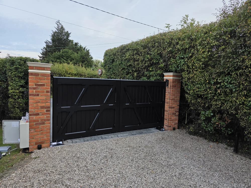 Black timber double swing driveway gates hung between brick pillars